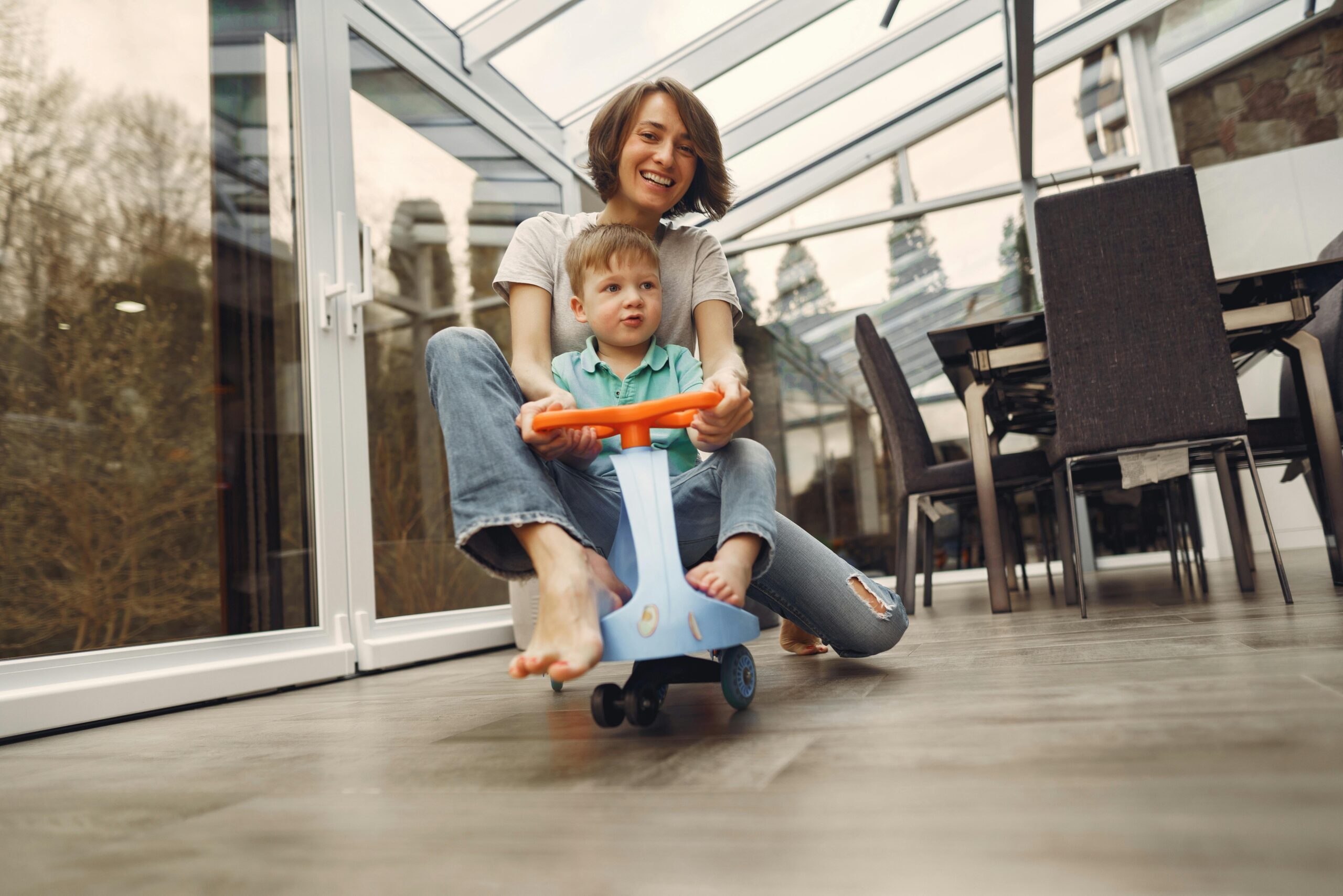 Pleated blinds A joyful mother and son bonding while playing on a toy car indoors in a bright conservatory.